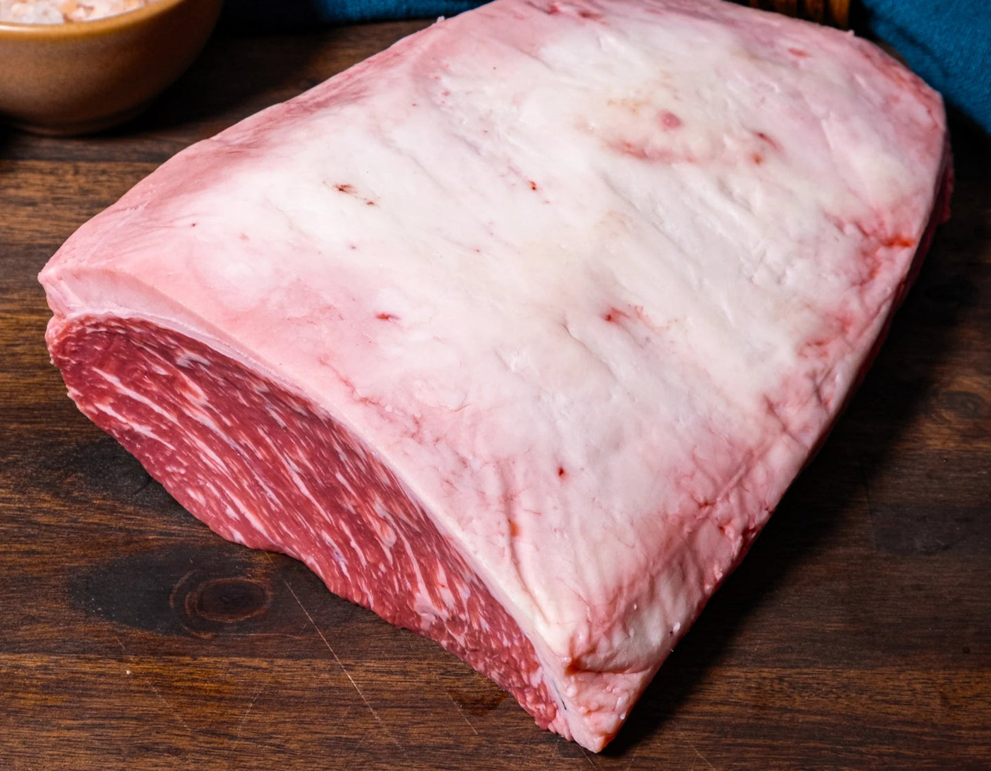 Raw meat on a wooden surface with a bowl of salt and a blue napkin.